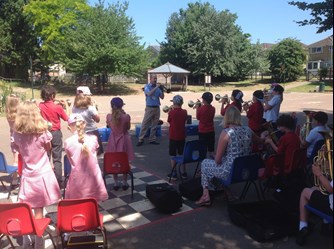 A photo of the pupils of Stratton Primary playing in their brass concert. They are facing away from the camera towards their teacher as he guides their playing.